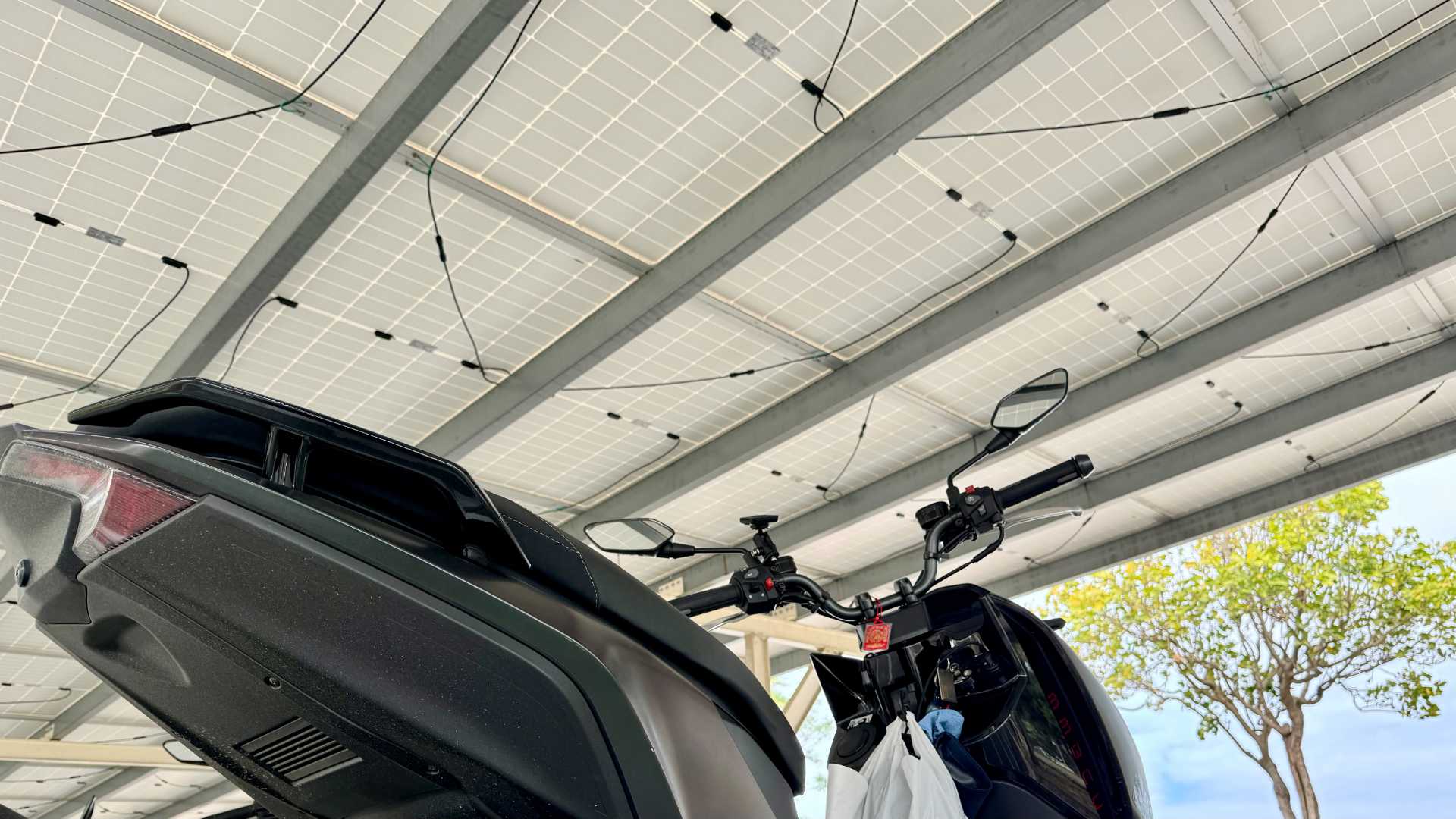 A motorcycle parked underneath new-looking solar panels with loose wiring.