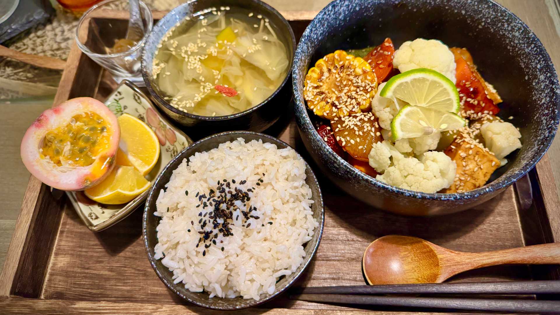 Tray of food including soup, rice, a bowl of braised vegetables, and a side of passionfruit.