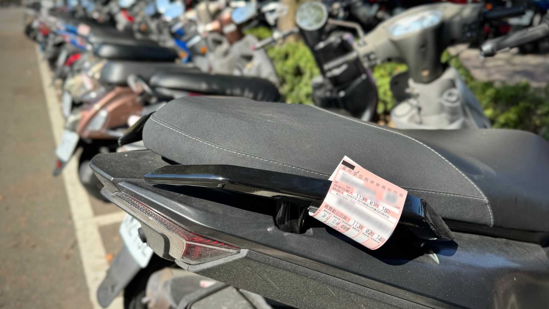 A parking ticket affixed to the rear handles of an SYM MMBCU scooter.