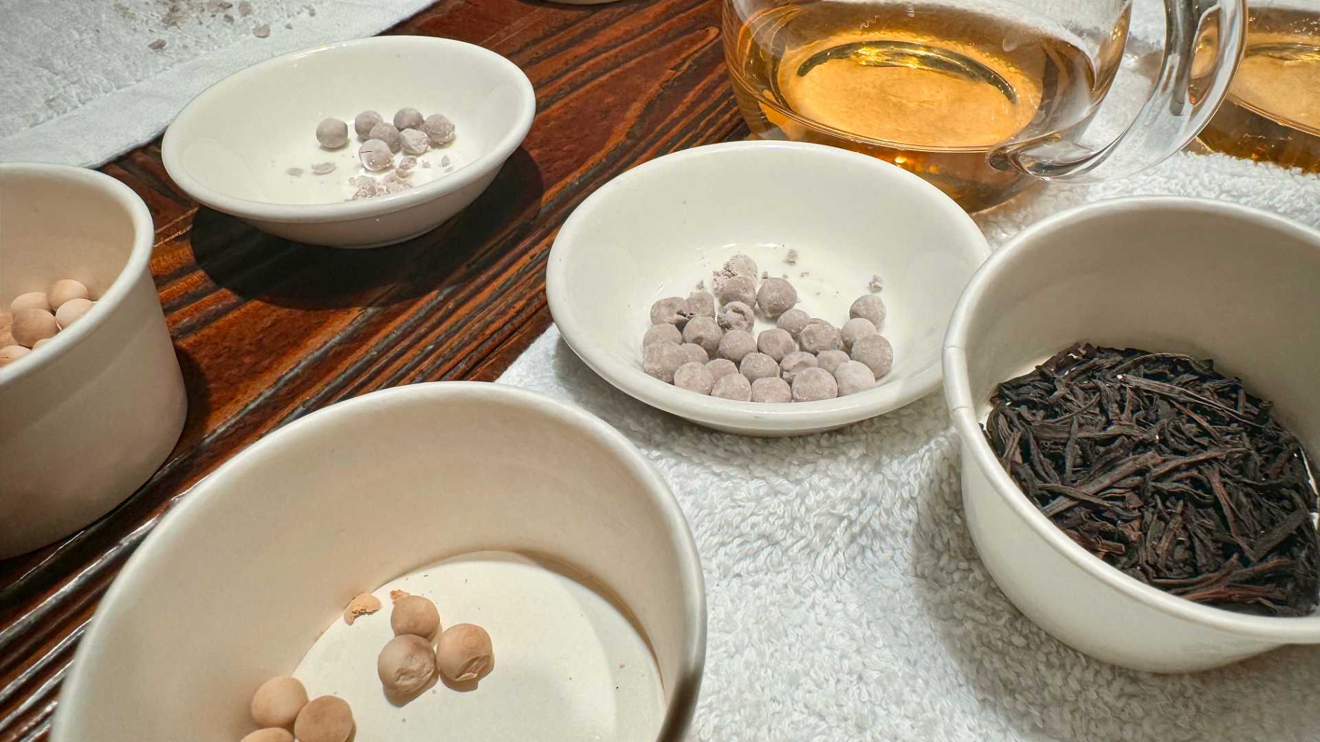 Bubble tea ingredients in container on a wooden table. Visible are black tea leaves, uncooked black and white tapioca balls, and liquid cane sugar.