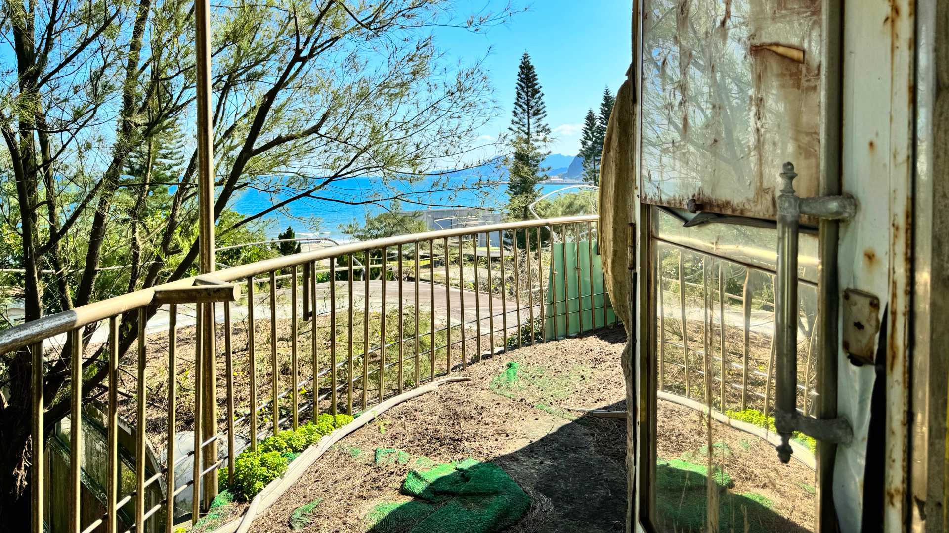 A curved deck around a deteriorating Futuro home, with a view of the East China Sea in the distance.