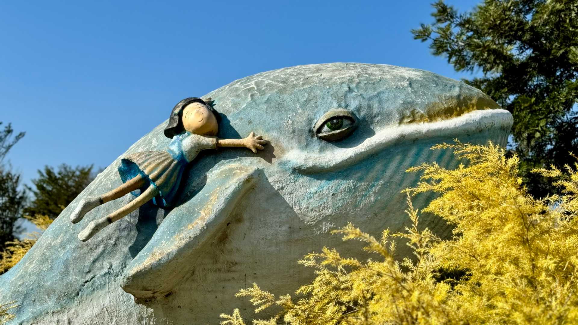 A sculpture of a girl hanging on the side of a whale. The sculpture is about 2 meters tall.