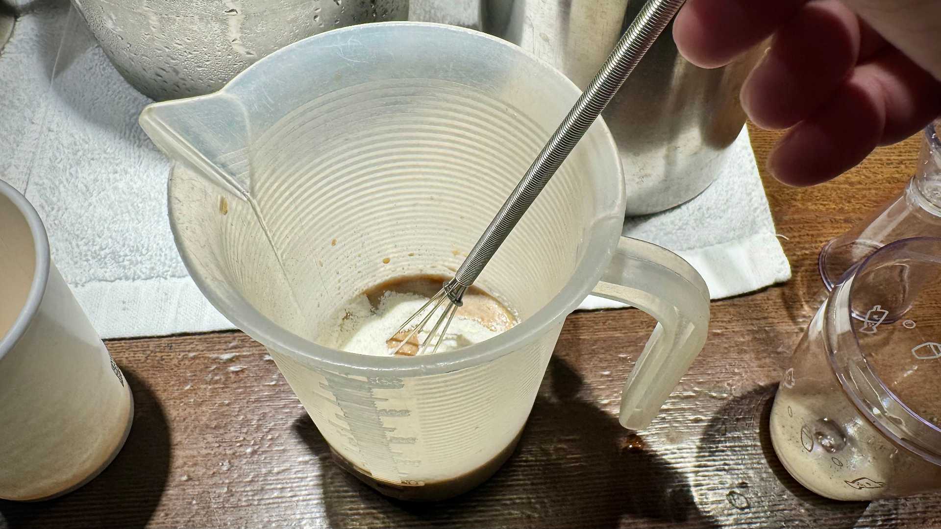 A small handheld whisk mixing black tea and creamer.