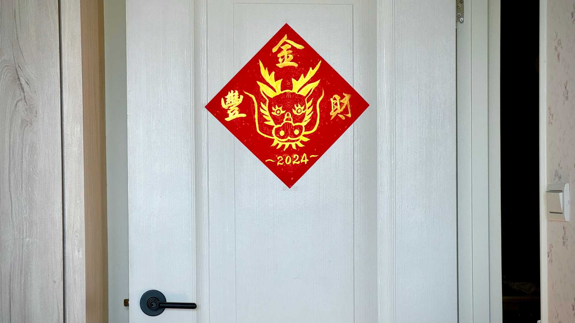 A diamond-shaped piece of paper decorated with a dragon head, the year ‘2024”, and three Chinese characters, affixed to a door.