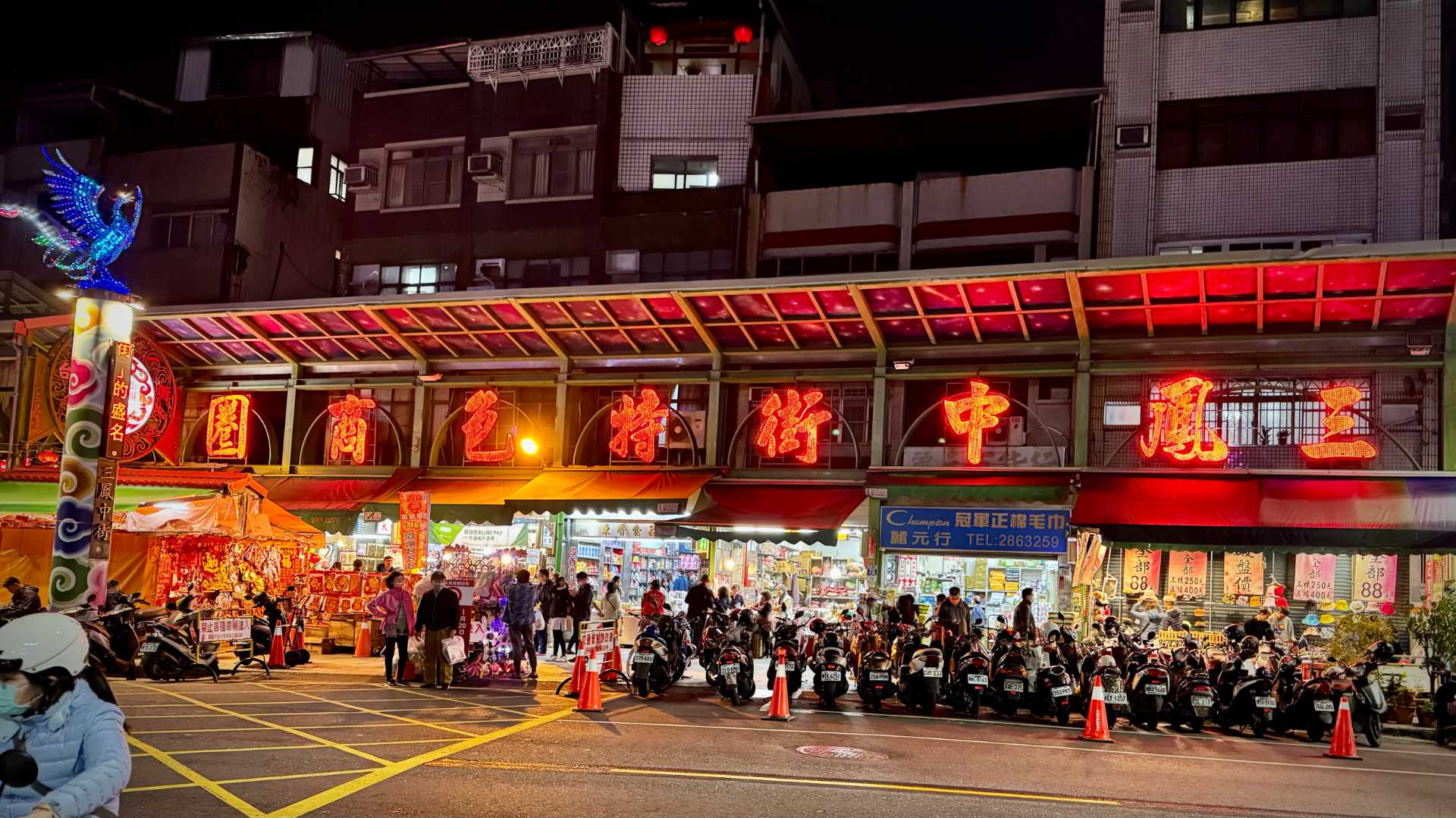 Sanfonzon Street entrance. Lots of scooters are parked outside small, crowded shops at night.