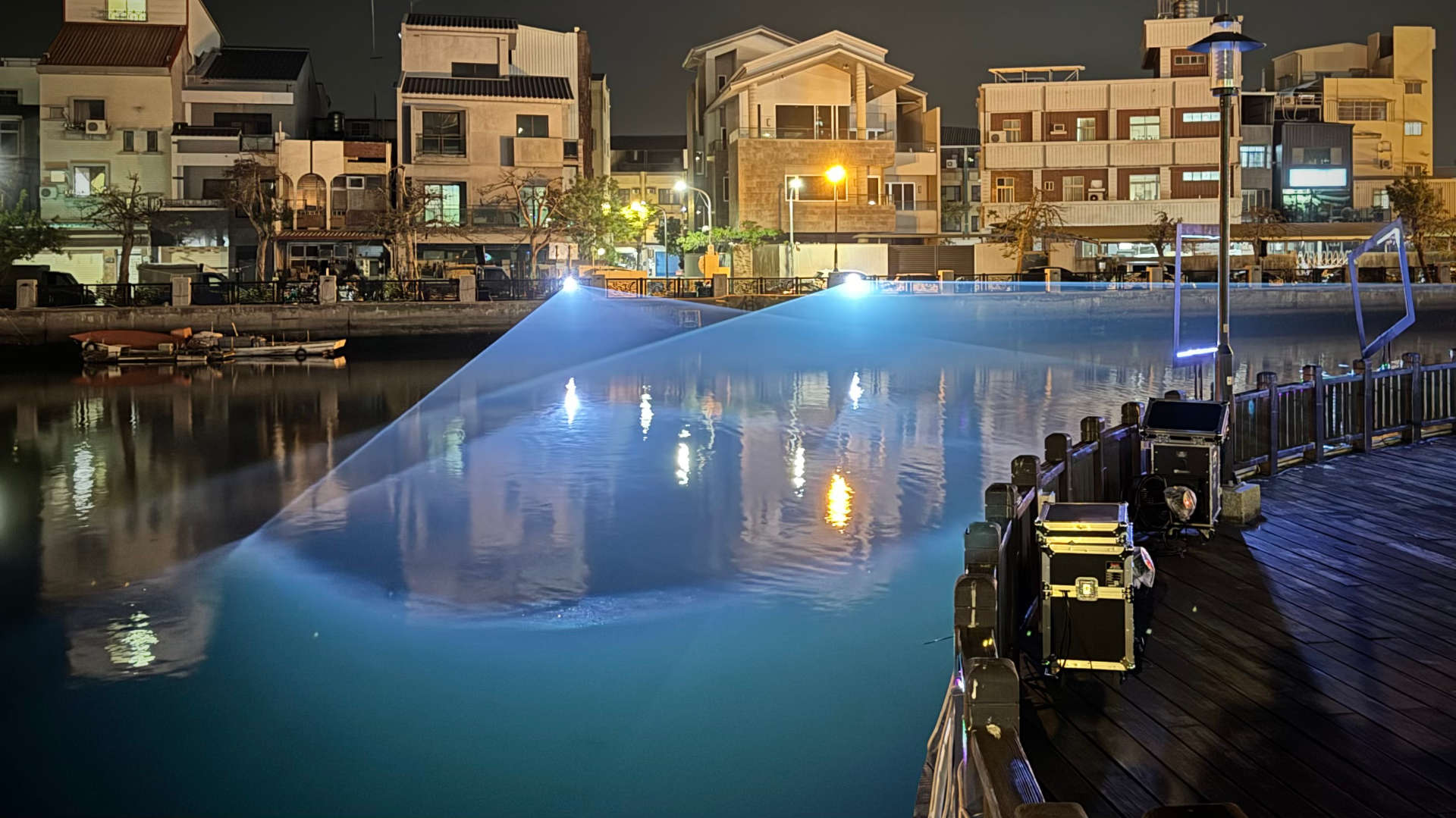 View across Tainan Canal to lazer projectors on the far side, projecting wide triangular beams of light over the water.