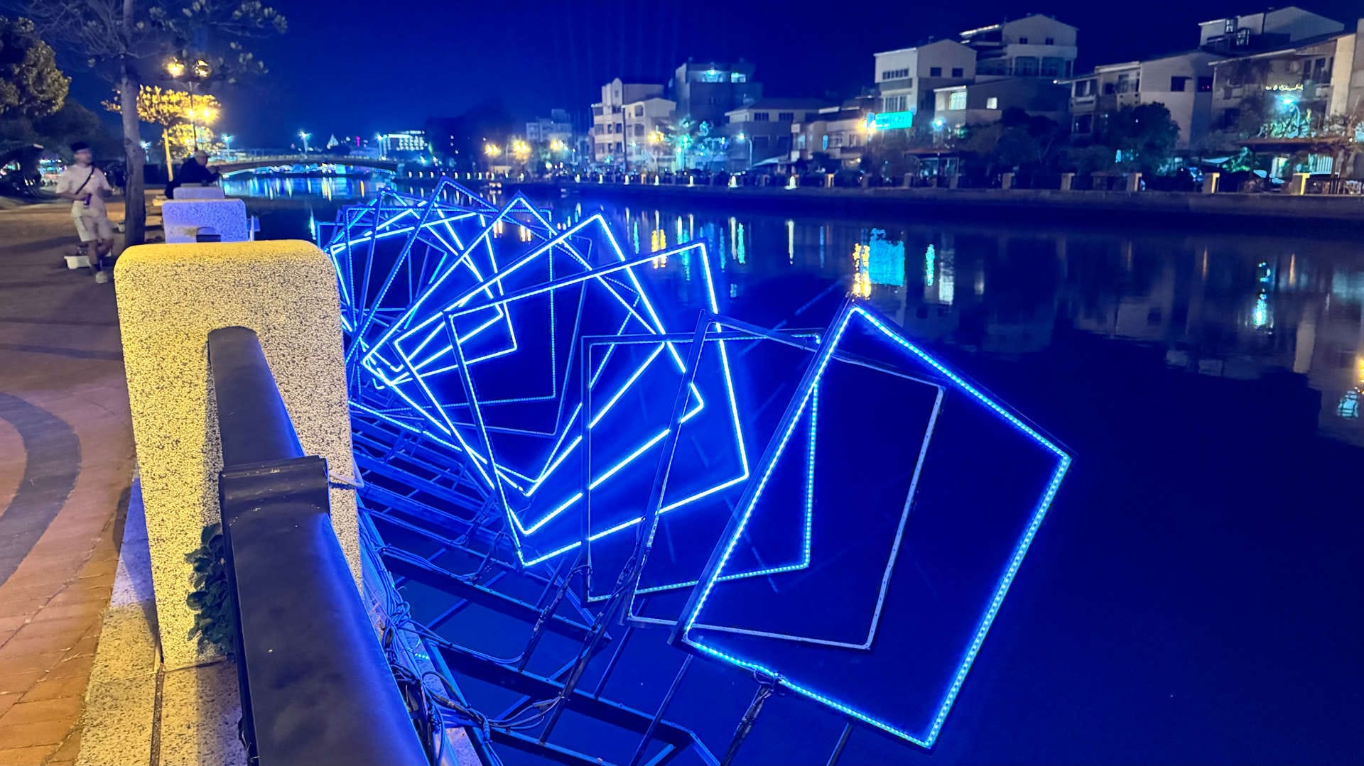 A series of illuminated empty square metal frames suspended over the side of Tainan Canal.