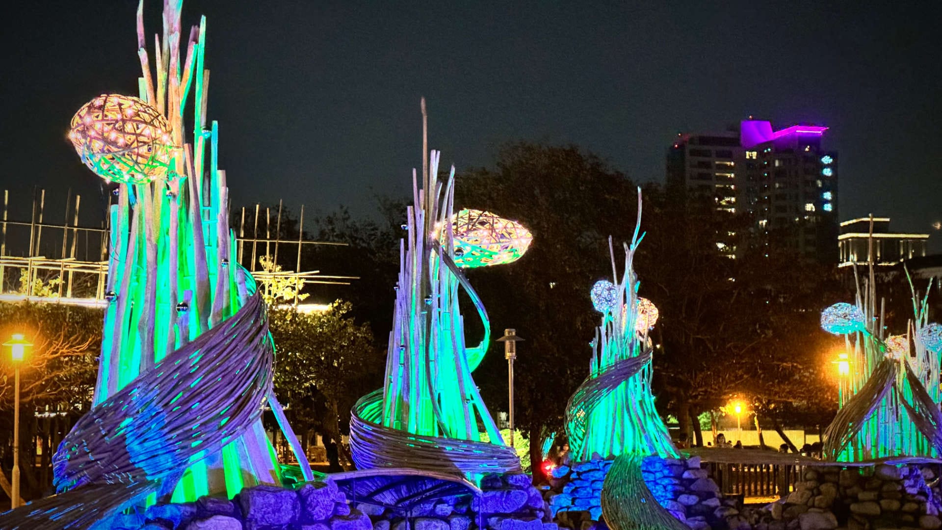 A series of illuminated tall abstract sculptures that have plant-like buds near the top.