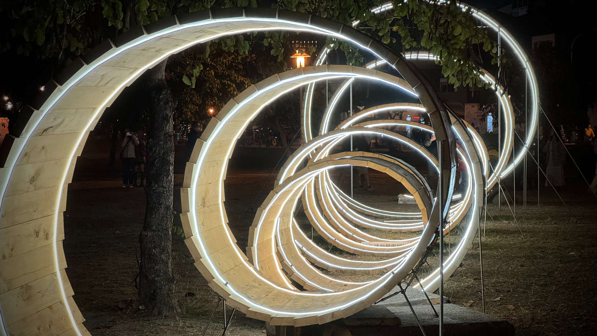 Illuminated sculpture of a 3D spiral stretched into the distance, made of wood.