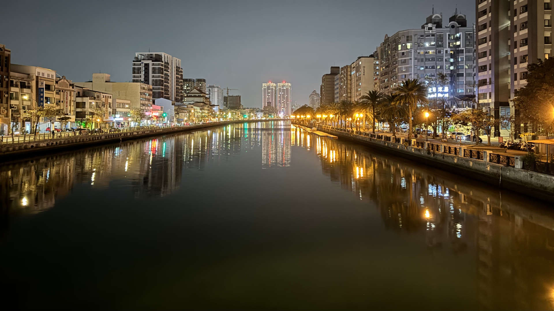 Photo taken from a bridge, looking up Tainan Canal at night. The water is still and reflective.