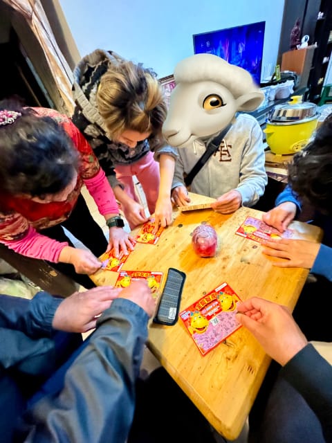 Six people sratching lottery tickets on a small square table. Their faces are not visible. One person’s face is obscured by a sheep emoji.
