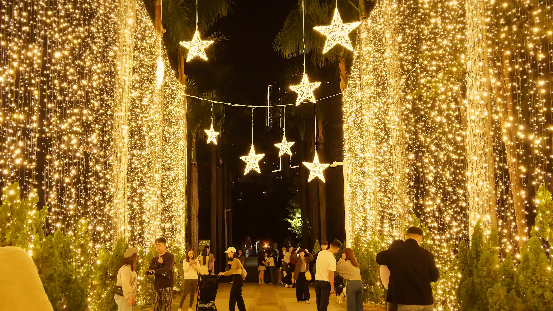 People walking underneath hanging stars made of dozens or hundreds of small lights.