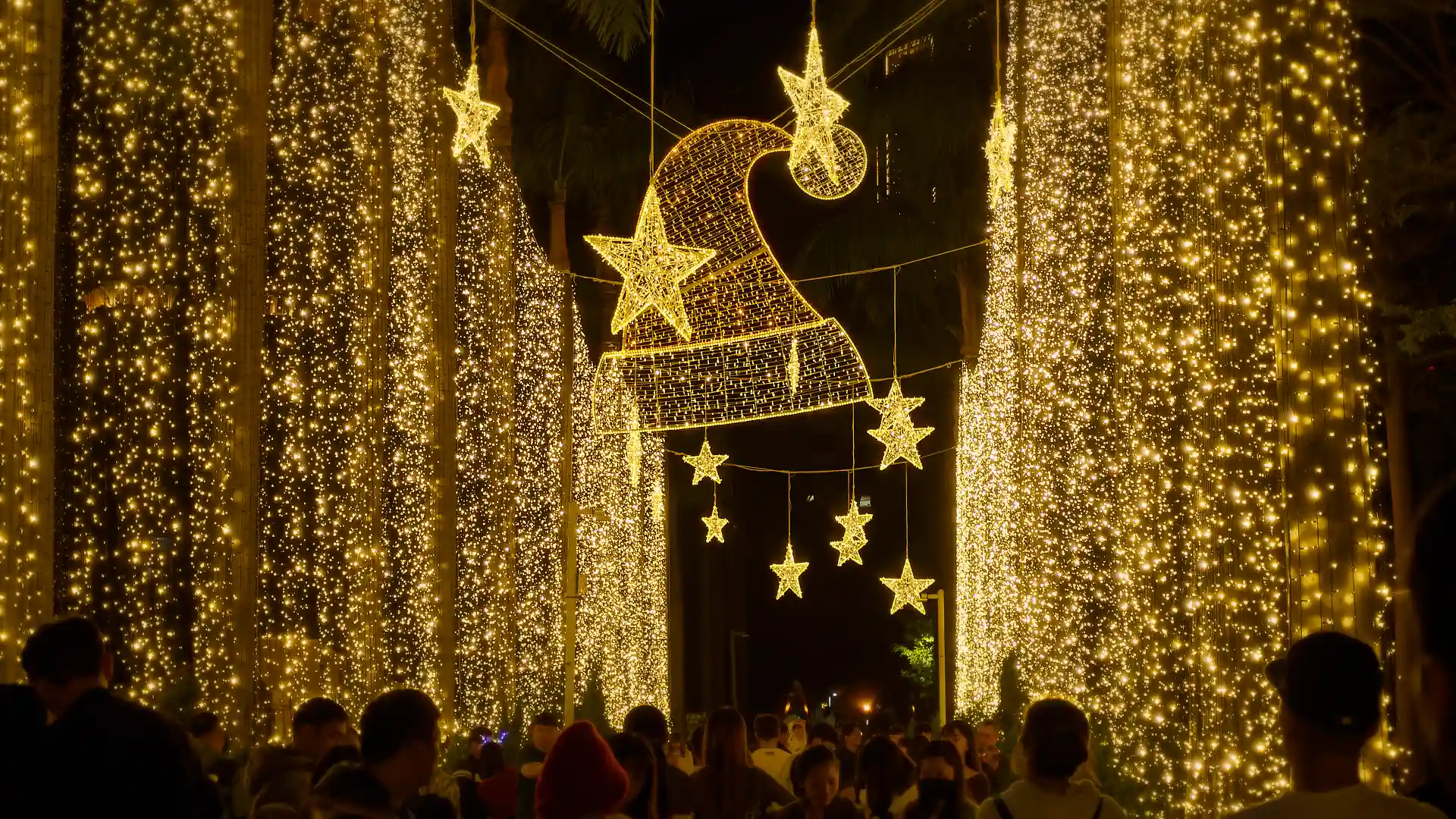 A large two-dimensional Santa hat made of hundreds of string lights, hanging above a crowd.
