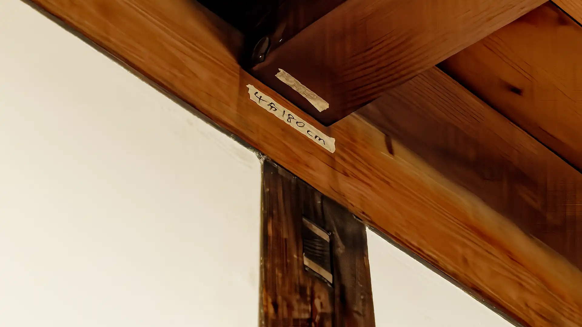 Close-up of some builder’s notes on masking tape, affixed to a horizontal beam. The note says 180cm.