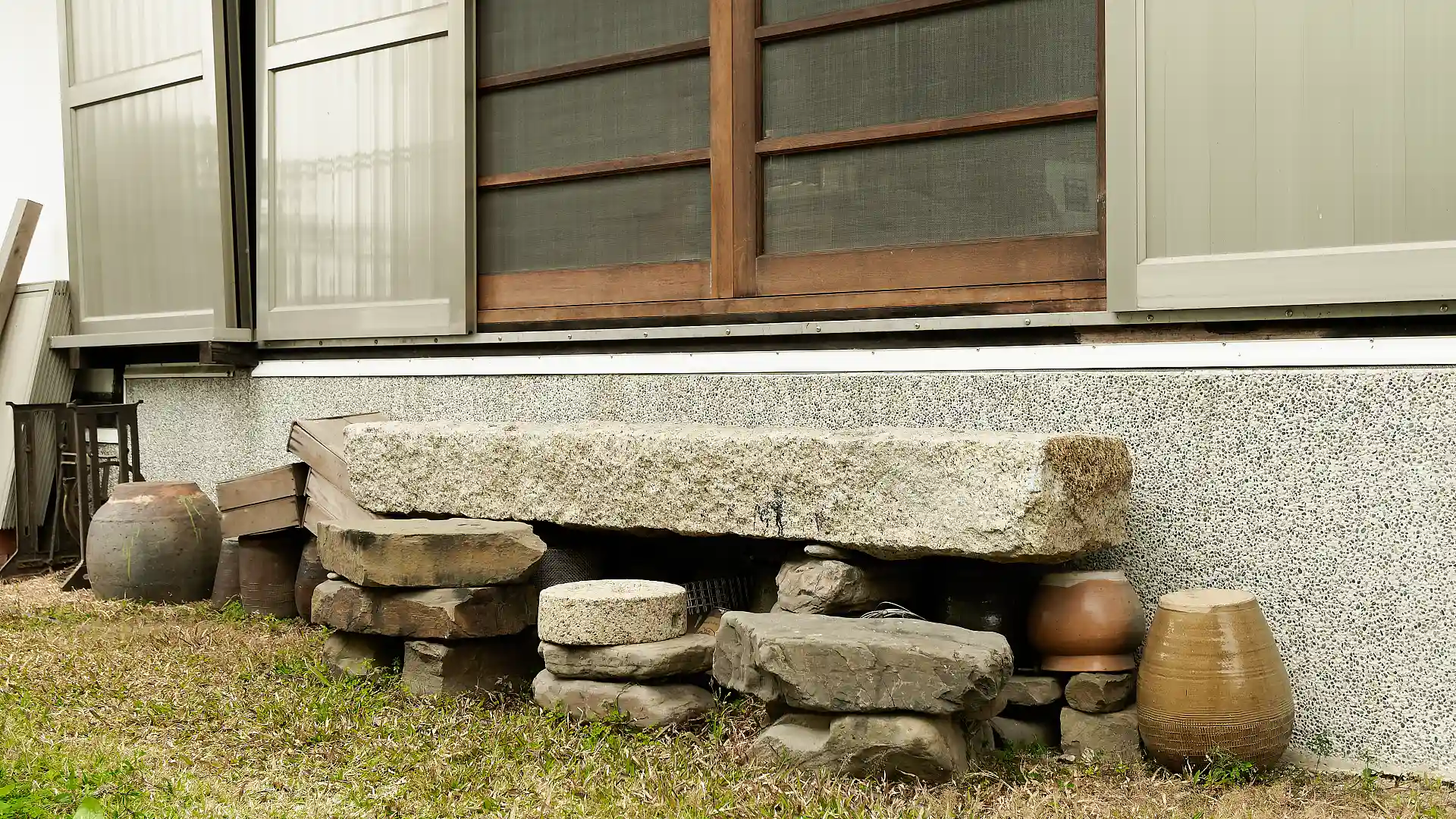 Exterior steps made of pieces of stone and paving and clay pots, beneath sliding wooden screens.