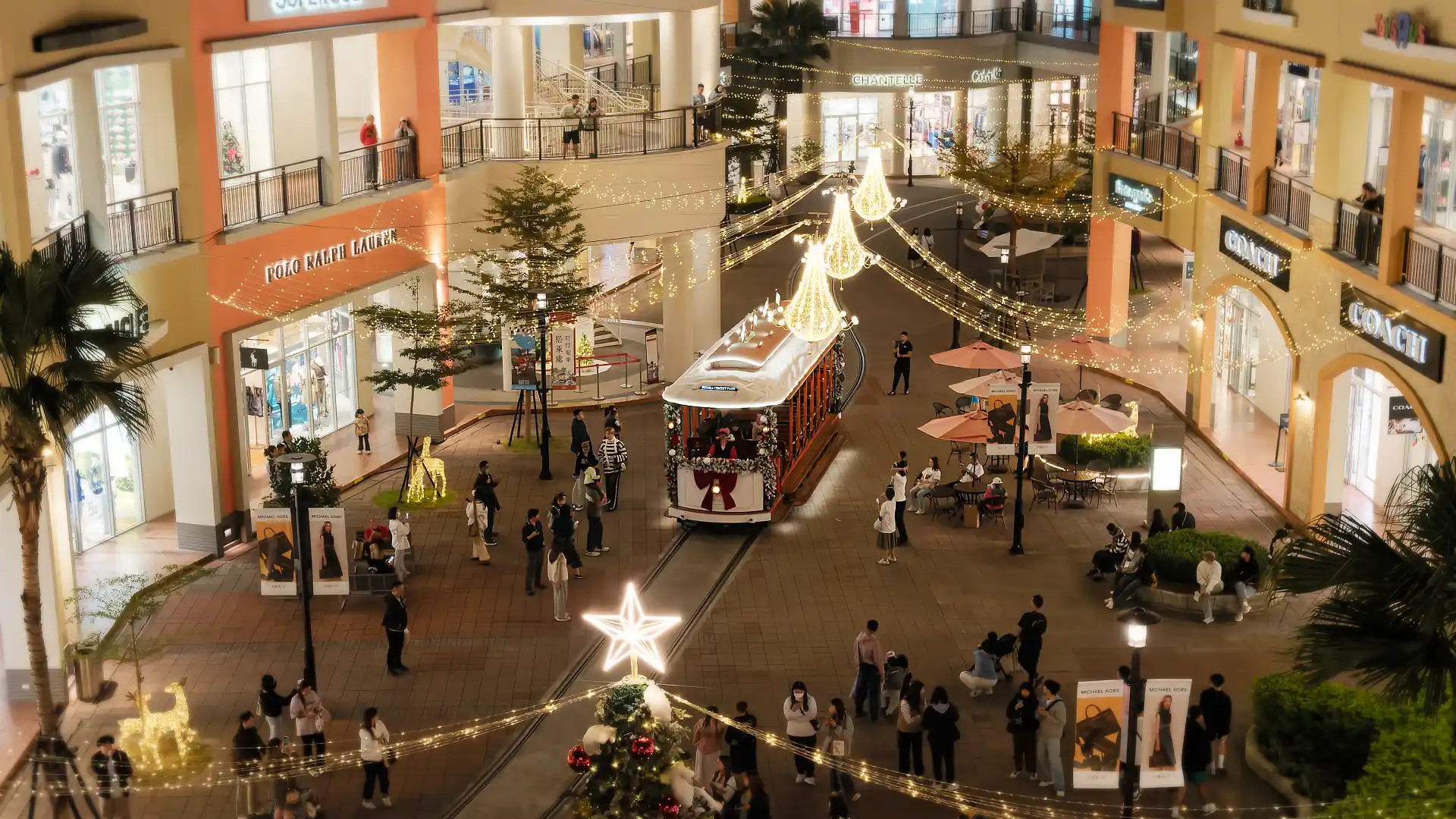 A tram (or trolley) moving through the outdoor square at SKM Park shopping mall. The tram and square are decorated in Christmas lights.