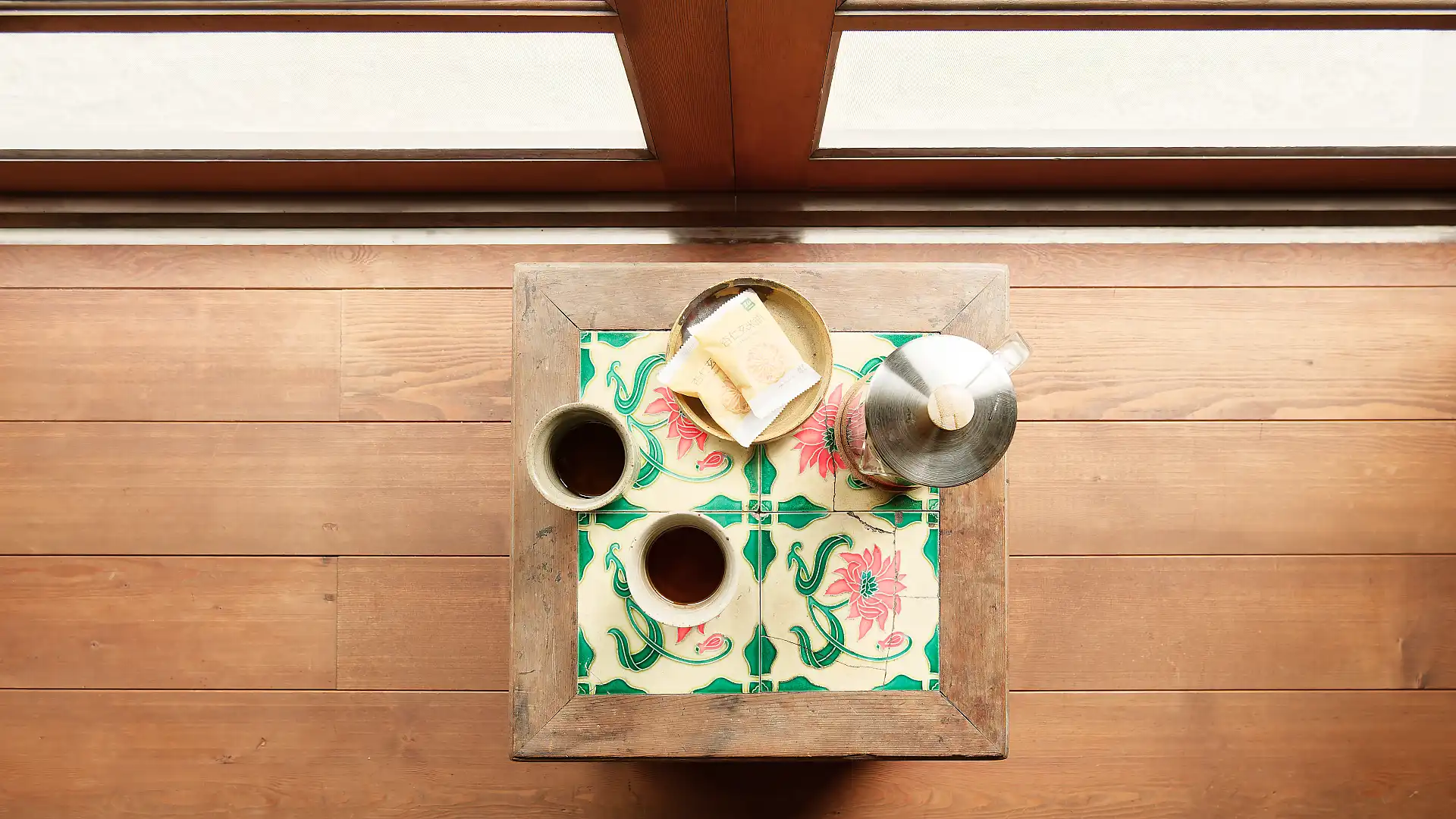 Top-down view of two half-full tea cups on a tiled side table.