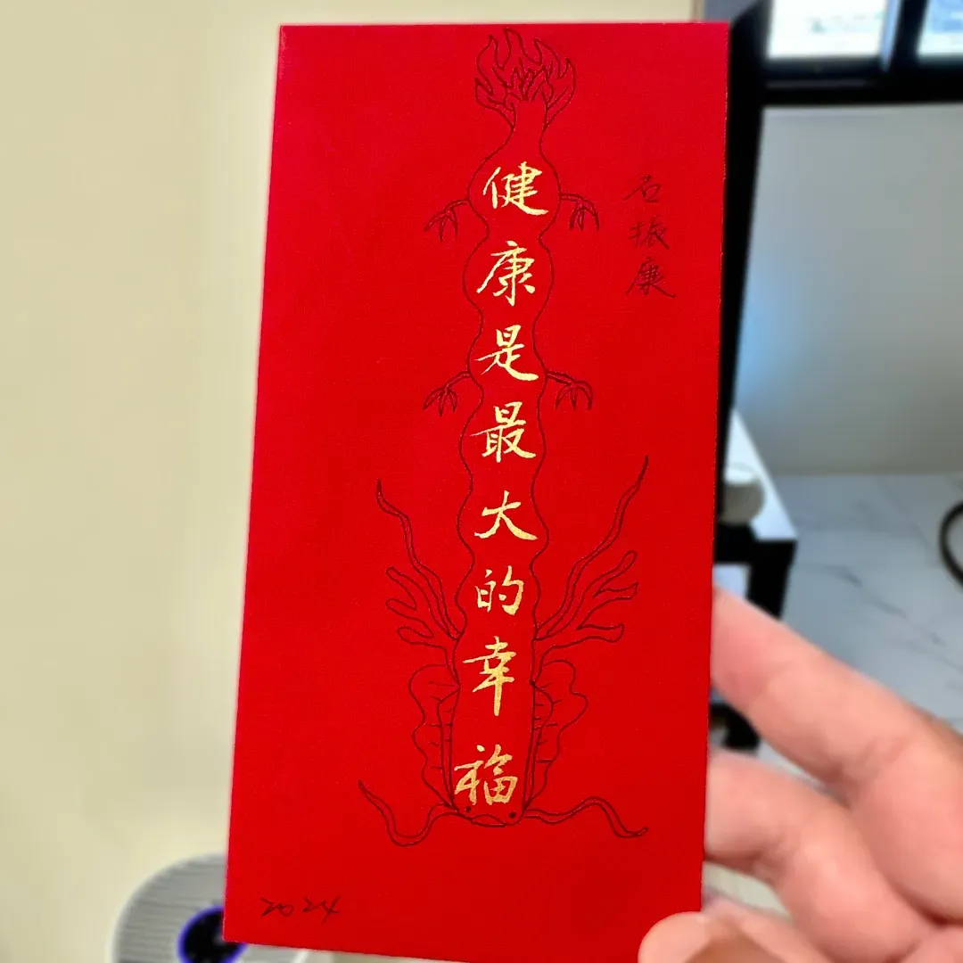 Hand holding a red envelope. In addition to printed Chinese characters, the envelope includes a hand-drawn dragon and the date “2024”.