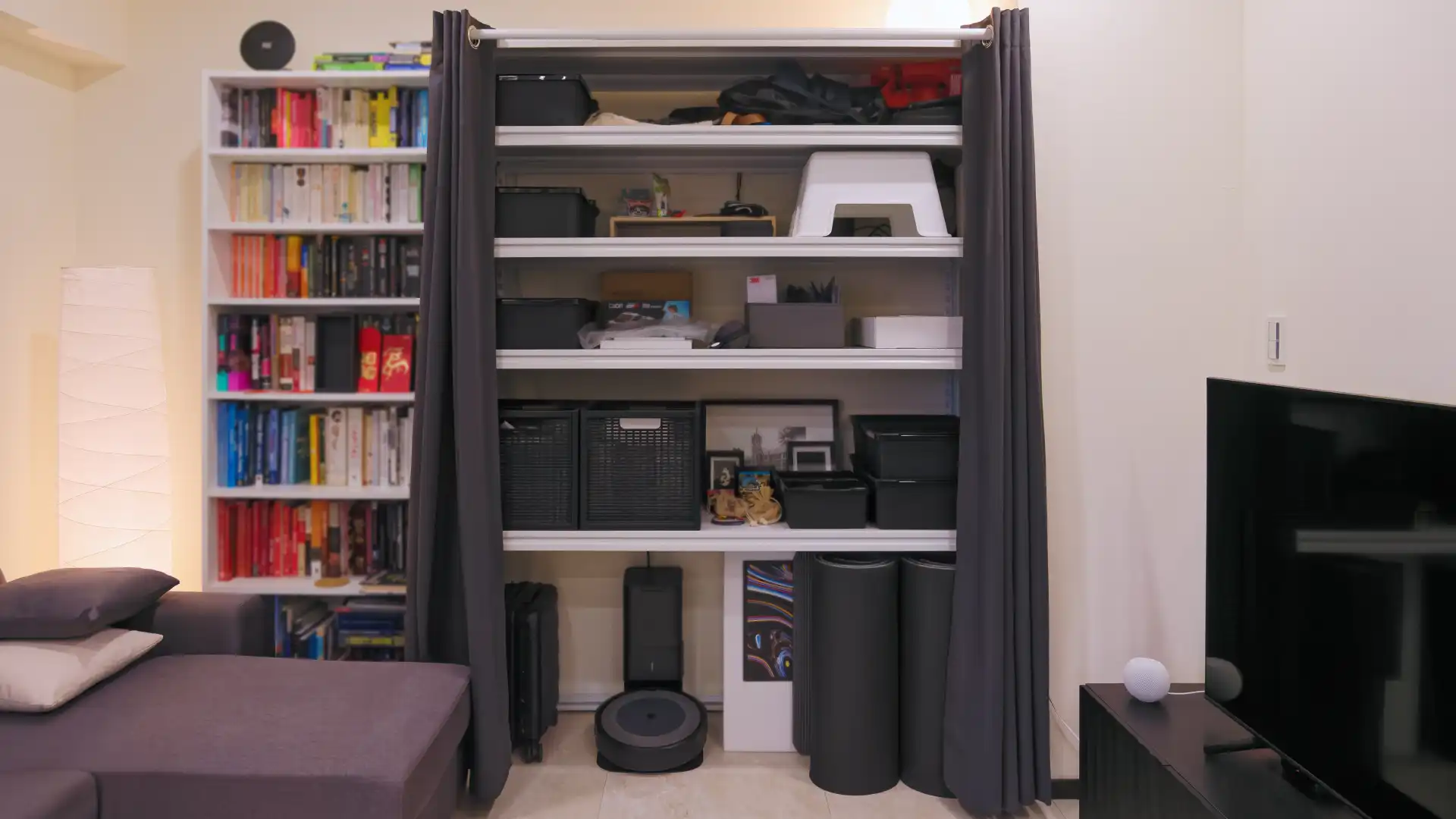 A large two-meter-tall metal shelving unit, with shelves full of household items and parted curtains across the front.