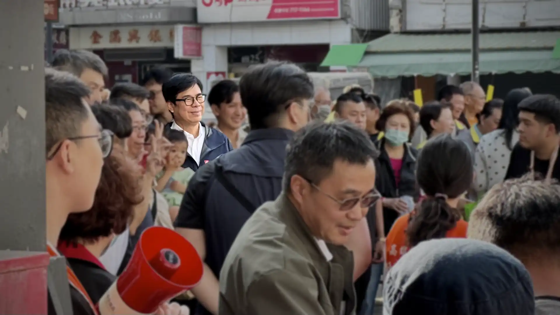 Kaohsiung mayor Chen Chi-Mai highlighted, with a crowd of people around him. A person in the foreground is holding a megaphone.