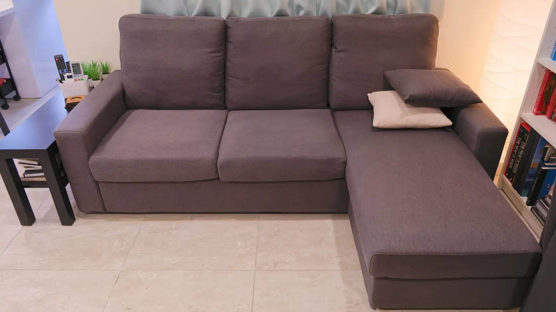 Three-seater gray fabric sofa with chaise extension on the right side, and two cushions.