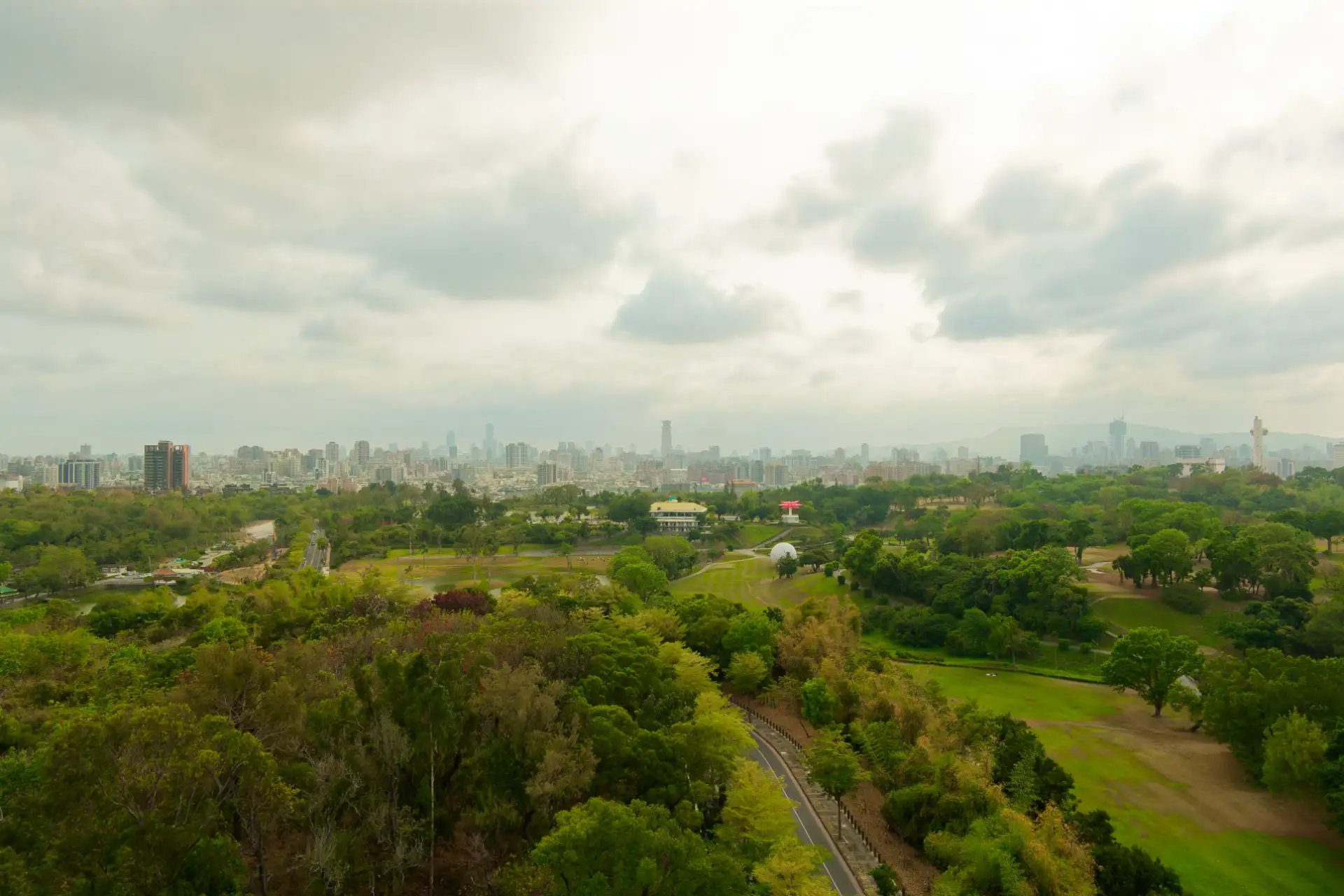 An expansive view across a forest and golf course in the foreground, with the skyscrapers of Kaohsiung visible in the distance.
