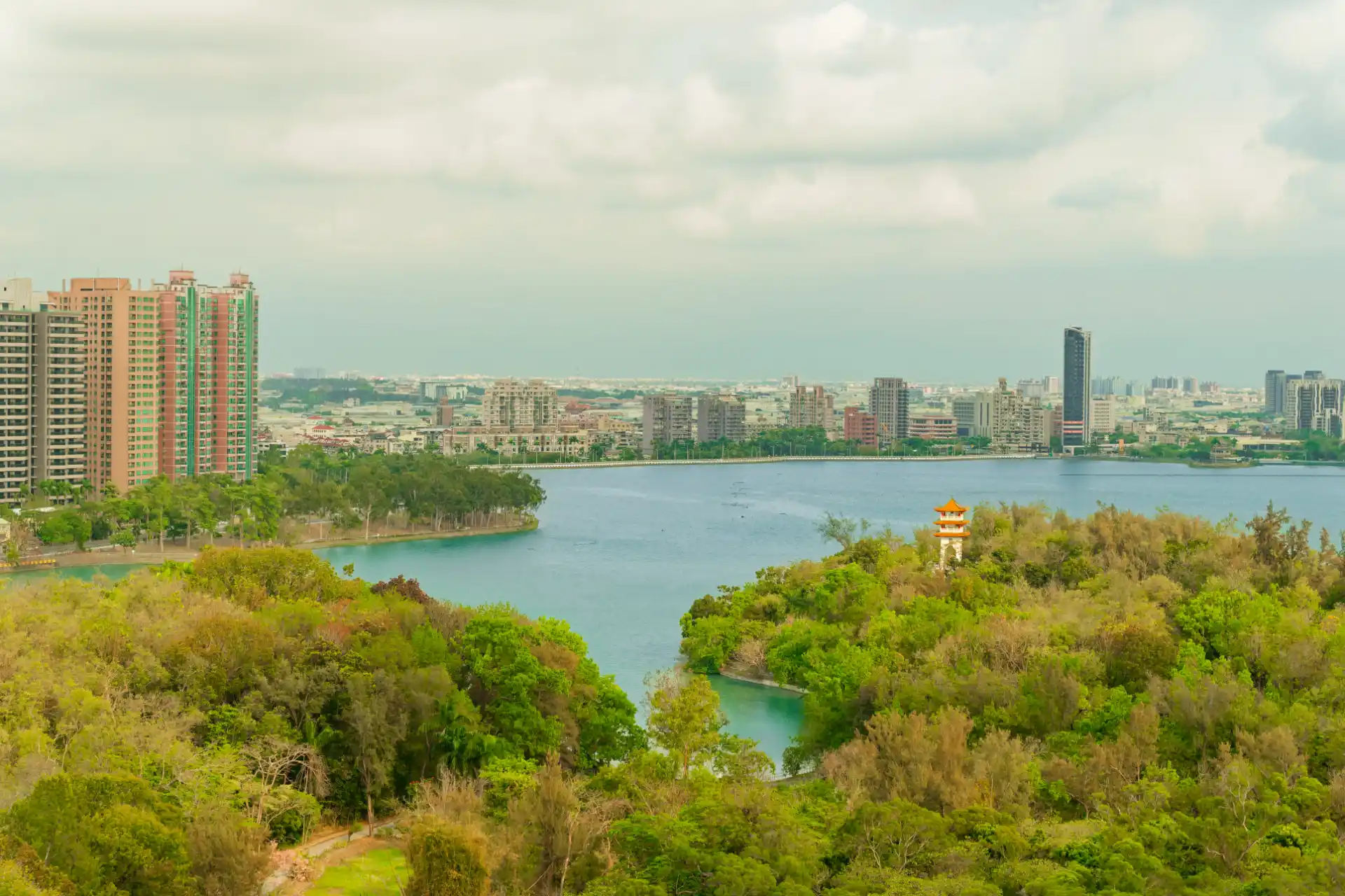 An expansive view over a forest and a lake, with mid-rise apartment buildings in the distance.
