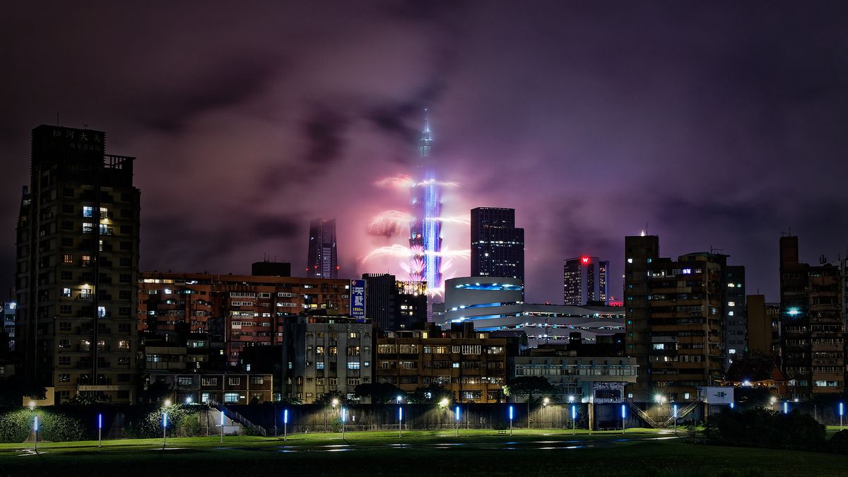 Fireworks launching from Taipei 101, with smaller buildings and Keelung River in the foreground.