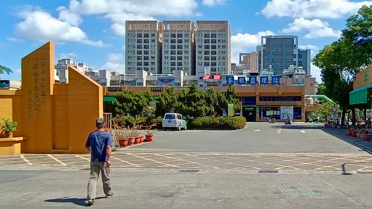 A man walks past the entrance to Kaohsiung City Motor Vehicles Office. It’s a sunny day.