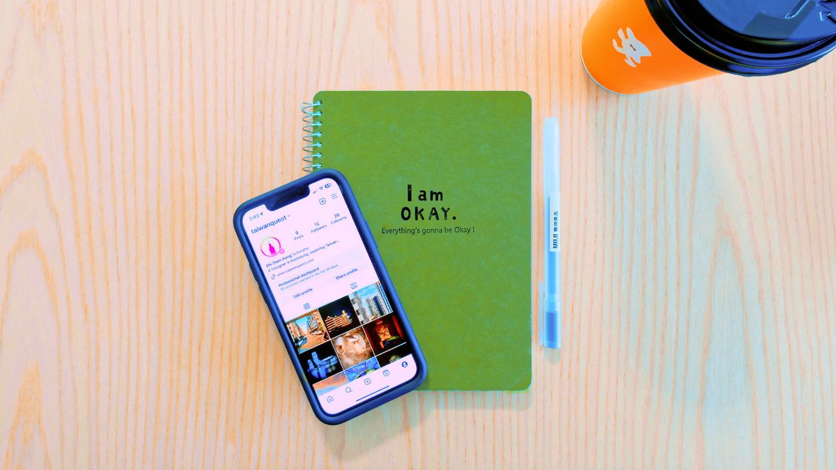 Phone, notebook, pen, and takeout coffee cup on a desk.