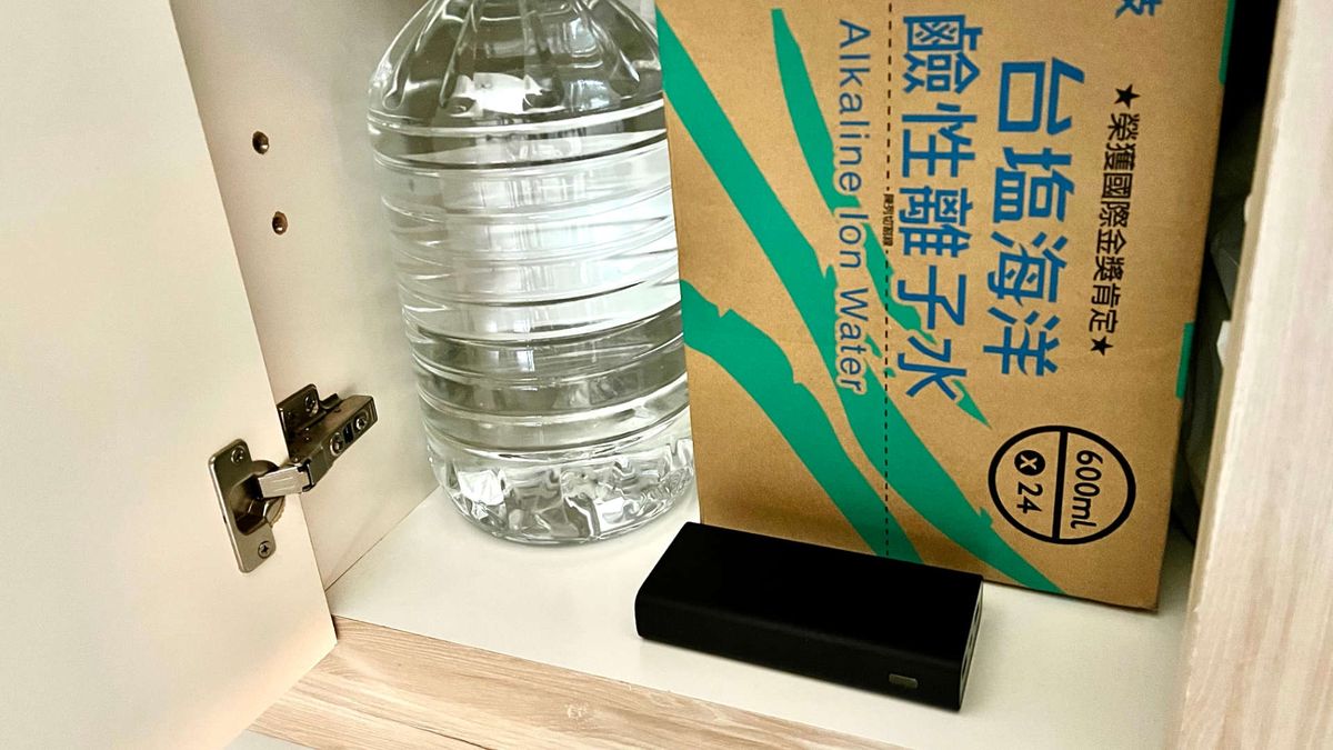 An open cupboard with bottles of water and a power bank inside.