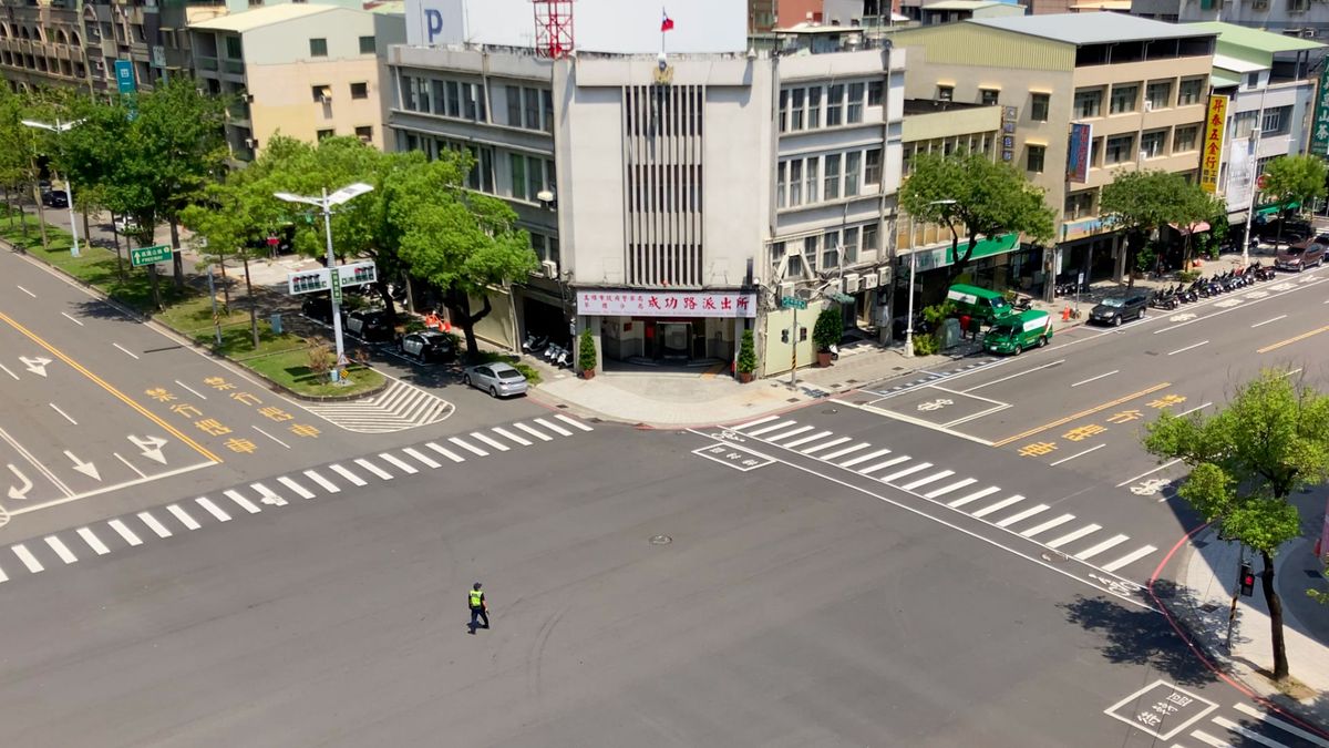 A police officer stands in the middle of an otherwise-empty intersection of two 6-lane roads.