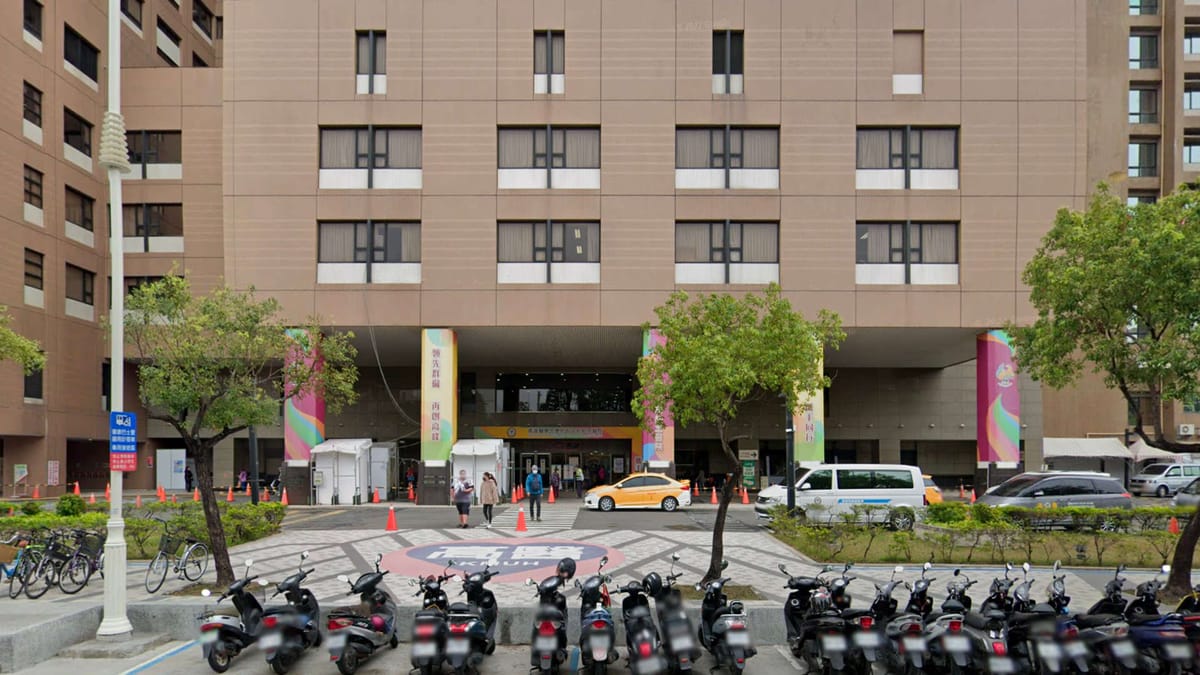 Exterior of a large hospital building, with taxis and scooters parked outside.