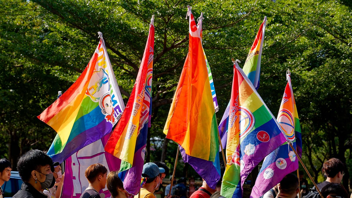 Group of people walking with rainbow-colored flags on a sunny day.