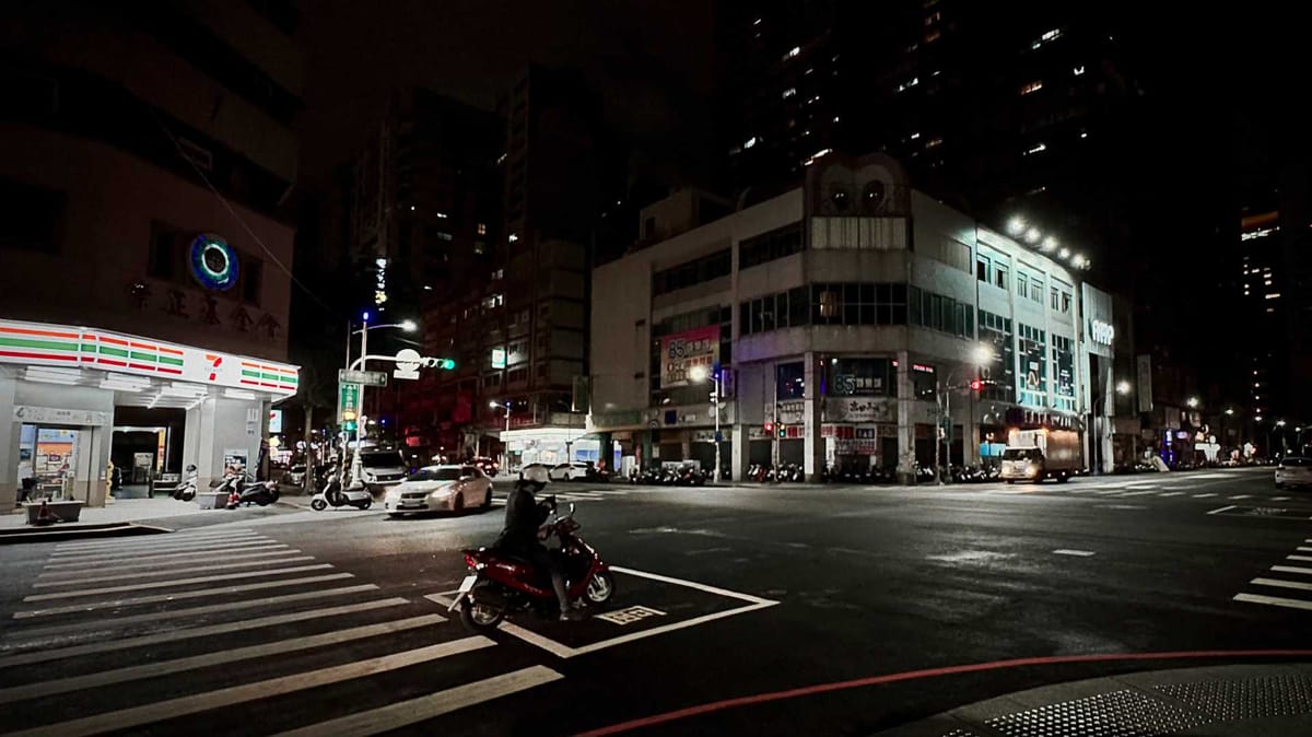 A night-time street photo of an intersection in Kaohsiung, Taiwan. A 7-Eleven is clearly visible across the street.