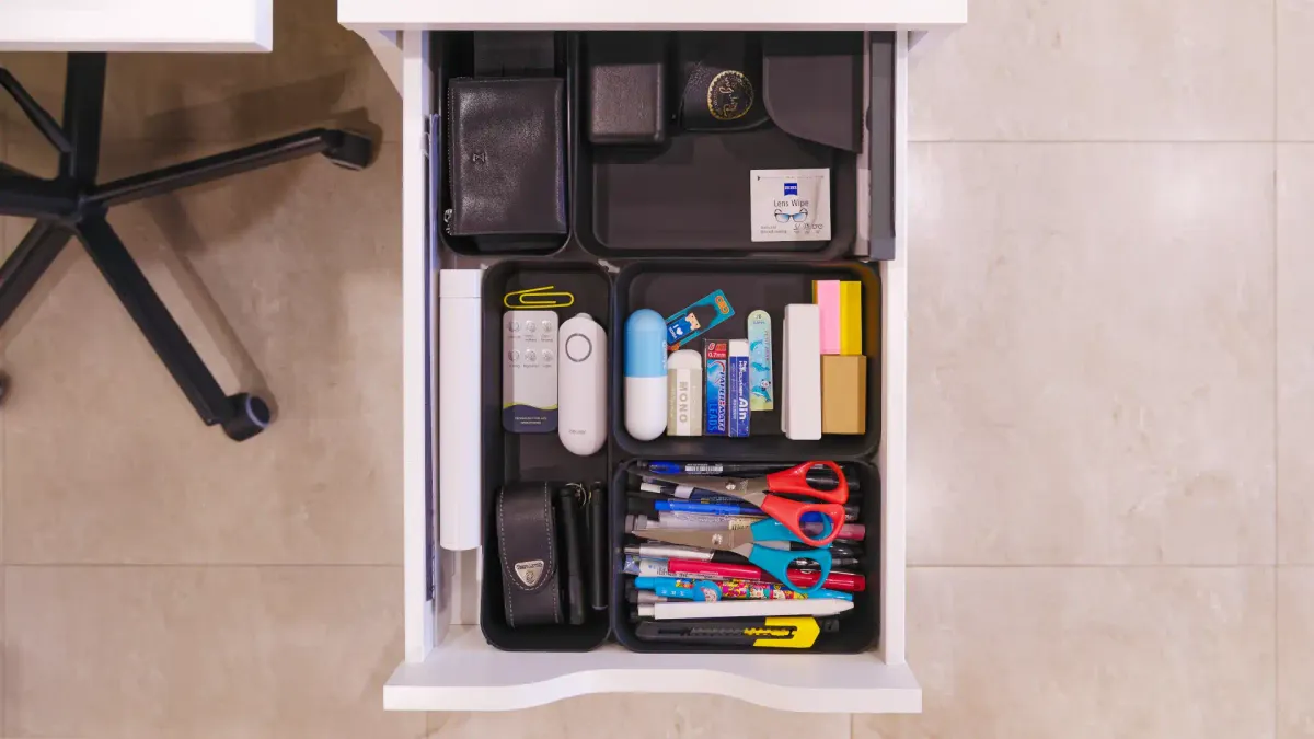 An open office drawer with stationery items in organizer trays.